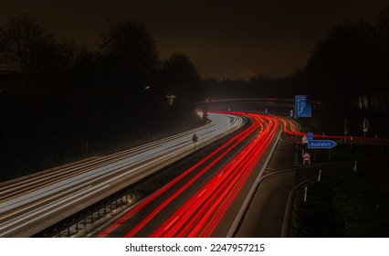Long exposure, white front and red rear lights as car light strips at night, German text for exit and diverse place names, Ausfahrt and diverse Ortsnamen - Shutterstock ID 2247957215