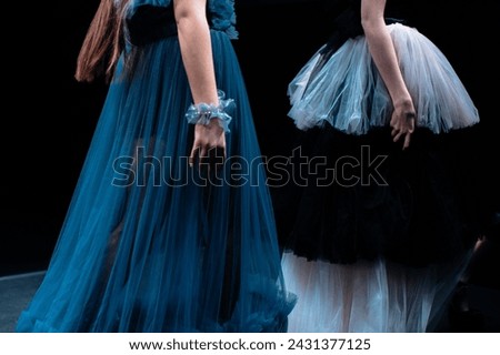 Long fluffy evening blue and white dresses on a female figures on a black background. Fashion show details