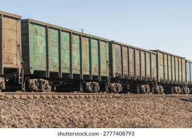 Long freight train moves through rural agricultural landscape at sunset. Lengthy convoy of freight rail cars traverses peaceful countryside under bright sunlight
