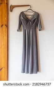 A Long Gray Bridesmaid Dress With Embroidery And Sequins Is On A Hanger On The Wall