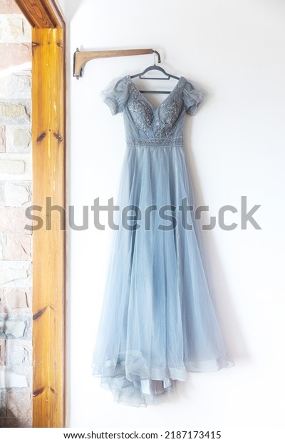 A long grey bridesmaid dress with\
embroidery and sequins is on a hanger on the\
wall