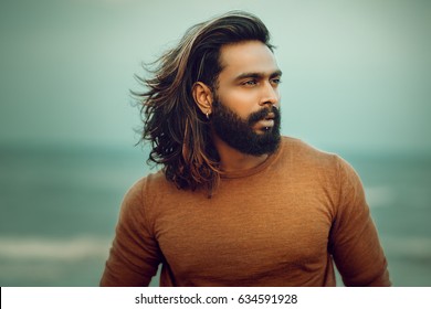 Long hair bearded young man portrait enjoying breezy wind in sea background.