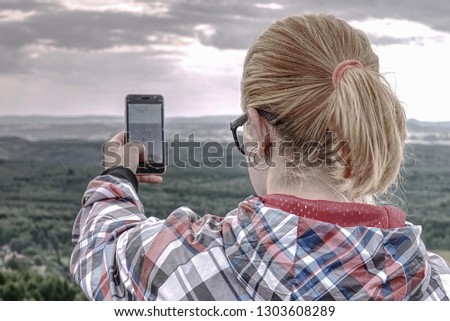 Long hair cute girl take picture by smart phone. Morning hilly landscapewith few clouds of mist.