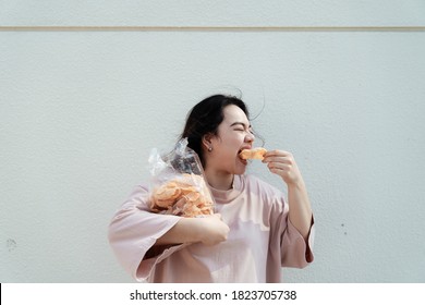 Long hair fat woman eat rice craker with wide mouth in front of white wall.