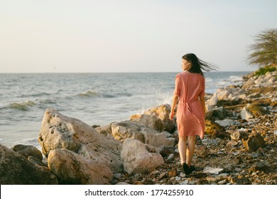 Long hair girl walking alone on the rock beach in windy day.