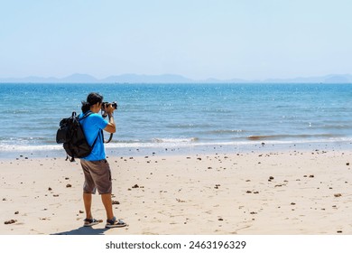 Long hair man wearing backpack take a photo of sea by digital camera on summer beach and blue sky  holiday trip. - Powered by Shutterstock