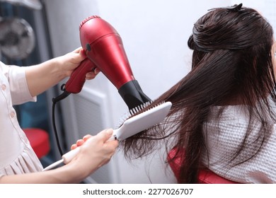 Long hair is styled with a hair dryer. A woman in a beauty salon. Long dark hair.Brush close-up. The concept of beauty salons.