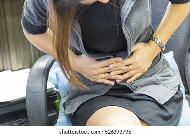 A long hair woman holding abdomen sitting at the desk.