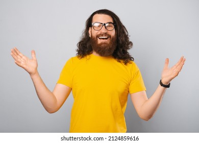 Long haired bearded man wearing glasses is staying with arms wide open. Studio shot over light grey background. - Powered by Shutterstock