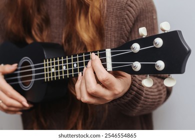 Long haired girl playing a black ukulele. Holding a chord on the fretboard with her hand. Musical performance in action. Black wooden musical instrument in focus. Artistic background of a musician. - Powered by Shutterstock