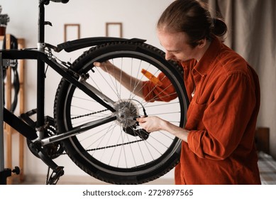 Long haired man using a wrench to repair bicycle rear wheel in apartment. Concept of DIY bicycle maintenance, home service, and transport repair. Professional tools for bike adjustment.