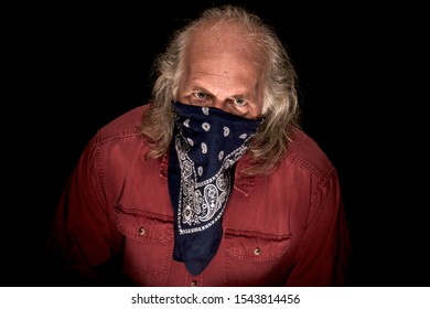 A Long Haired Masked Bandit Wearing A Blue Bandana To Cover The Face And A Red Shirt Glaring At Viewer With Dark Background.