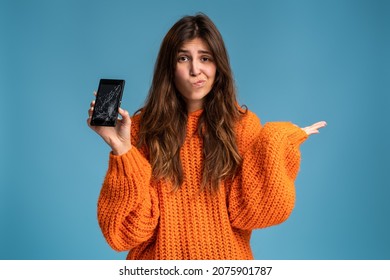 Long haired upset woman holding a out-of-use smartphone with broken screen and throw up hands in disbelief 