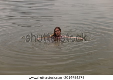 Long haired woman in pink dress swimming in the lake