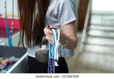 A Long Haired Woman Wearing A Blue Gray Shirt Held A Blue And White Necklace That Can Contrast Perfectly. She Was Reaching Into The Jewelry Box For Another Necklace.