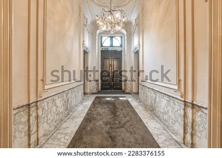 a long hallway with marble flooring and gold trim on the walls, along an ornate doorway leading to another room