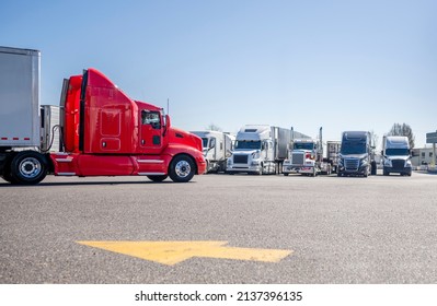 Long haul bright red big rig semi truck with extended cab transporting cargo in dry van semi trailer driving on truck stop parking lot with direction of movement arrow and row of another semi trucks - Shutterstock ID 2137396135