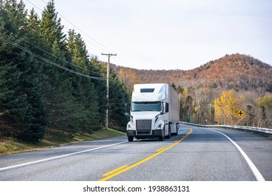 Long hauler professional industrial white big rig semi truck tractor transporting commercial cargo in dry van semi trailer running on the winding autumn road with mountain in New England