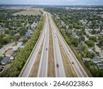 Long highway with cars driving on it and houses in the background. The houses are spread out along the sides of the road, with some closer to the highway and others further away