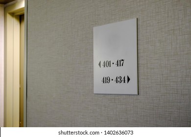 Long Hotel Hallway In Grey Colors With Room Numbers And Navigational Signs