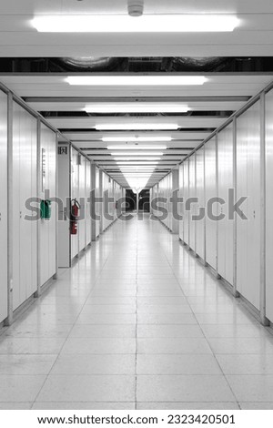 Long interior empty corridor hallway illuminated by neon lights with locker doors across both side, no people.
