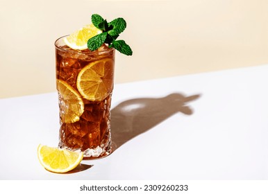 Long Island ice tea cocktail drink with vodka, rum, tequila, gin, liquor, lemon juice, cola and ice with lemon slice and mint in highball glass. Beige background, hard light, minimalism 