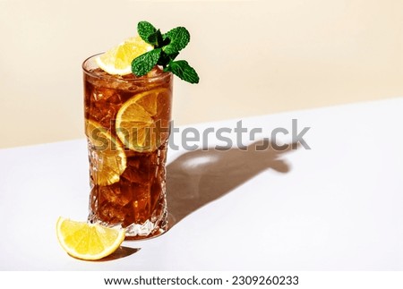 Long Island ice tea cocktail drink with vodka, rum, tequila, gin, liquor, lemon juice, cola and ice with lemon slice and mint in highball glass. Beige background, hard light, minimalism 