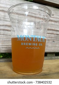 Long Island, NY - Circa 2017: Montauk Brewing Company Branded Sample Tasting Cup With Dark Amber Beer Inside Sitting On Outside Wood Bar Counter. Illustrative Editorial