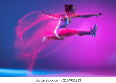 Long jump. Young athlete, runner training isolated on blue studio background in mixed pink neon light. Sportive girl in white sportswear practicing in run or jogging. Healthy lifestyle concept. - Powered by Shutterstock