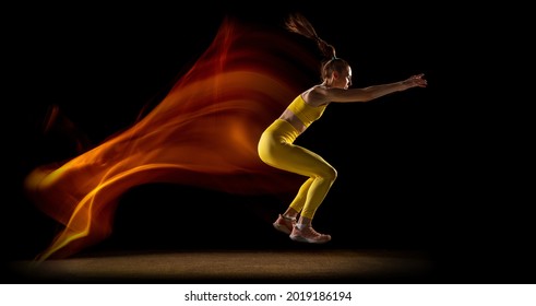 Long jump. Young woman, female professional track athlete jumping, landing isolated over black studio background in mixed neon lights. Concept of sport, healthy lifestyle, motion. Copy space for ad. - Powered by Shutterstock