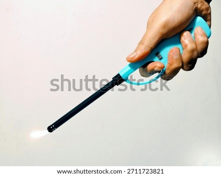 Long Kitchen Lighter Igniting a Small Flame, Held by a Hand Against a White Background