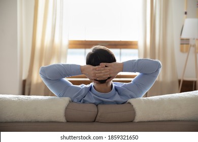 Long lasting plans. Rear view of successful millennial male businessman resting at home sitting on sofa with hands behind head looking at window creating new ideas dreaming of future opportunities