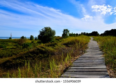 Long leading lines are created by the narrow boardwalk through the sand dunes at Kohler Andrea Park in Wilson and Sheboygan Wisconsin area with beautiful clouded skies in the late summer afternoon.