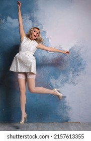 Long legged blonde photomodel in white minidress and white stockings posing at the studio  Beautiful smile, incredible leg