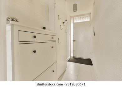 a long narrow hallway with white walls and black handles on the cabinetd drawers there is a plant in the corner - Shutterstock ID 2312030671