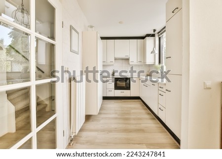a long narrow kitchen with white cabinets and appliances on the wall, as seen from the doorway leading to the dining area