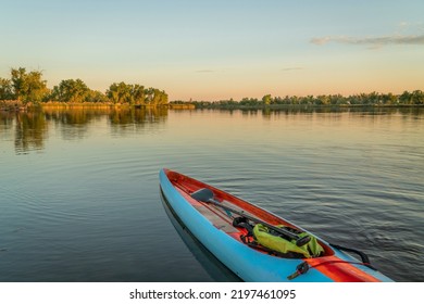 Long And Narrow Racing Stand Up Paddleboard With A Paddle And Safety Leash On A Calm Lake At Sunset.