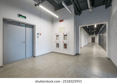 A long office corridor with a green emergency exit sign above a gray door. Loft-style 
decor. - Powered by Shutterstock