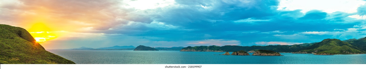 long panorama of evening colorful sunset in ocean coast of the Russian resort area of the Sea of Japan with hills and greenery, clouds on background  