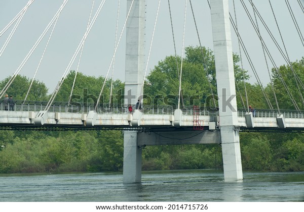 Long\
pedestrian bridge suspended by ropes across the river. Panorama of\
the bridge from the flooded embankment of the river. Suspension\
bridge on the background of the cloudy\
sky.