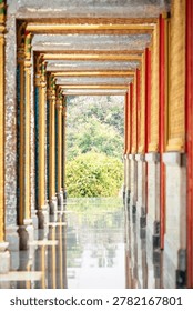 Long perspective corridor inside a Thai temple featuring golden frames, colorful columns, and symmetrical Buddhist architectural details.