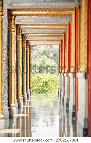 Long perspective corridor inside a Thai temple featuring golden frames, colorful columns, and symmetrical Buddhist architectural details.