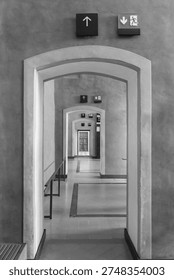 A long perspective view through multiple arched doorways in a modern museum interior with vibrant red walls and green exit signs