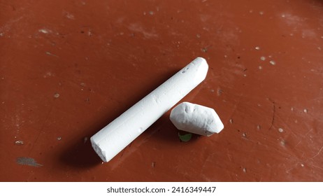 A long piece of white chalk sits on a brown base