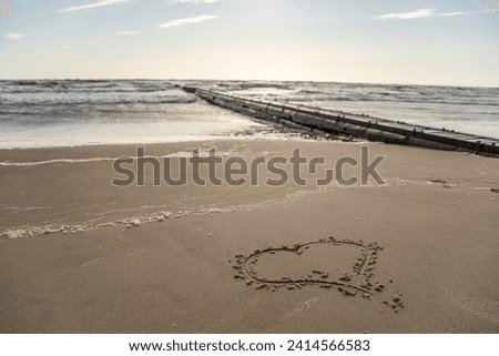 Long pier boardwalk leading out onto a Baltic sea, sunrise long way out with heart drawn in sand.
