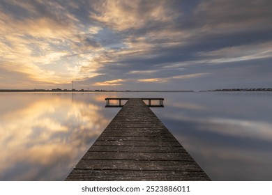 Long pier in a calm lake near Den Oever is surrounded by beautiful clouds. The rising sun has just enough space to beautifully illuminate the cloud cover. A photo to dream away to. - Powered by Shutterstock