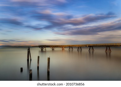 A Long Pier Stretching Out At A Misty Ocean At Sunset