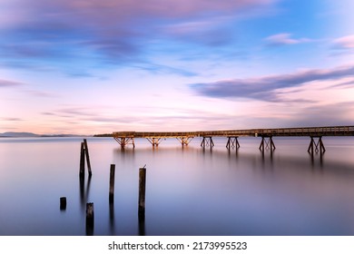 A Long Pier Stretching Out At A Misty Ocean At Sunset