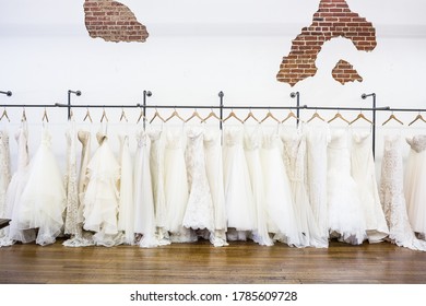 Long rack of wedding dresses on mostly white background in bridal shop.