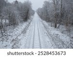 long railroad track leading onwards winter day with snow and forest on both sides of the track